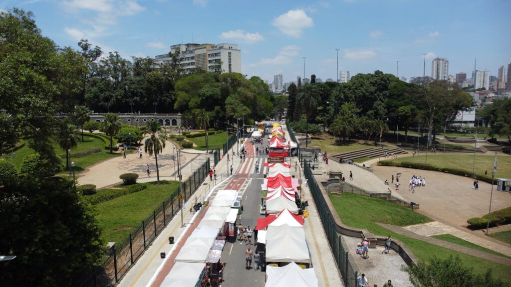 A lively outdoor market with colorful tents set up along a pathway in a vibrant urban park.